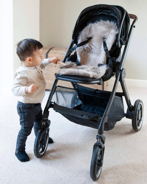 Child interacting with a stroller with sheepskin pram liner