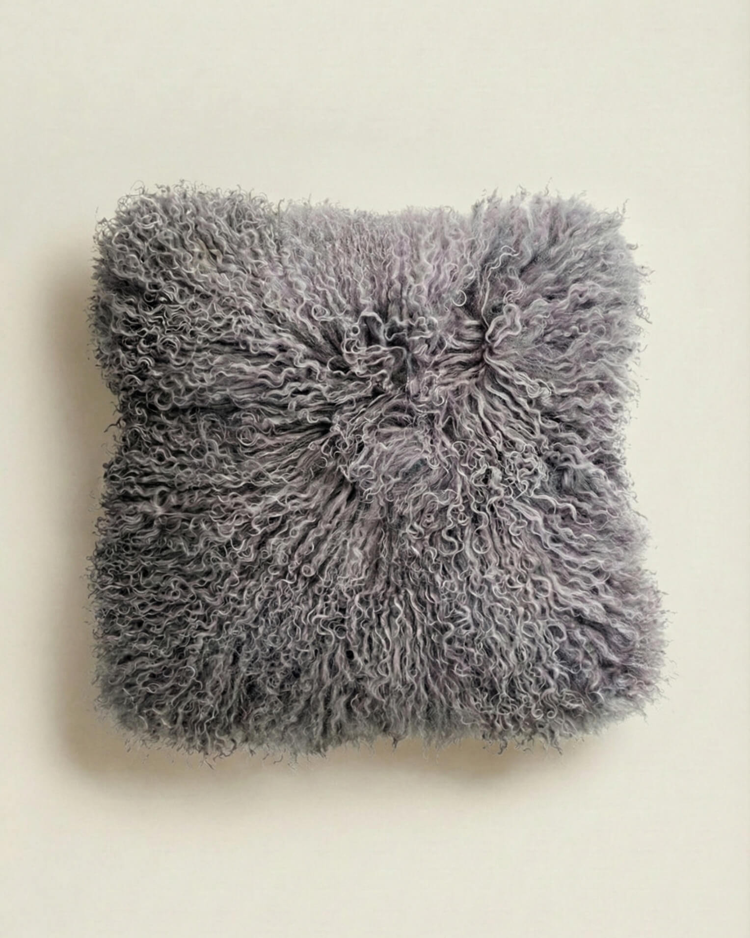 Fluffy grey mongolian sheepskin pillow on a beige background