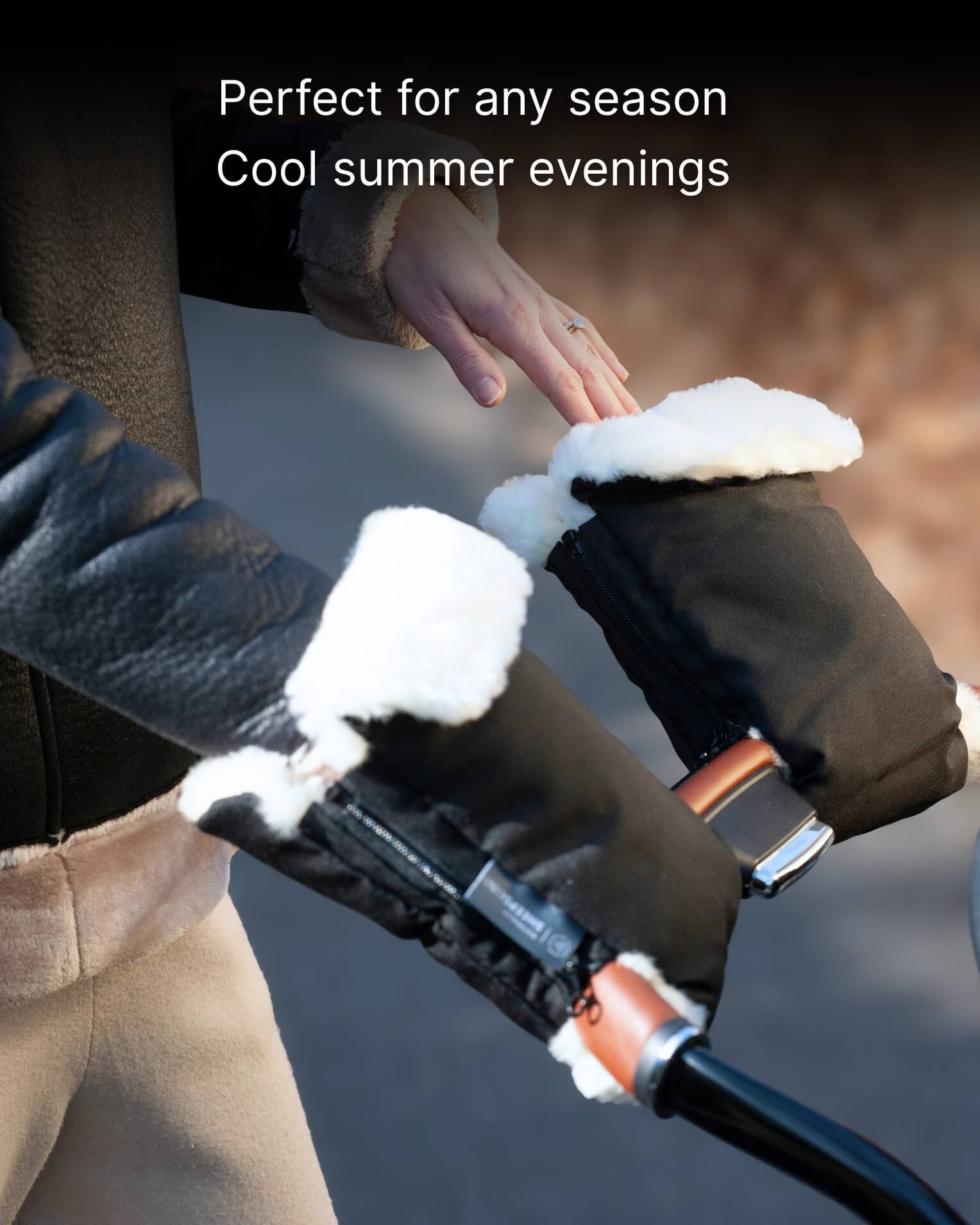 Person wearing black sheepskin gloves with white fur lining pushing pram.