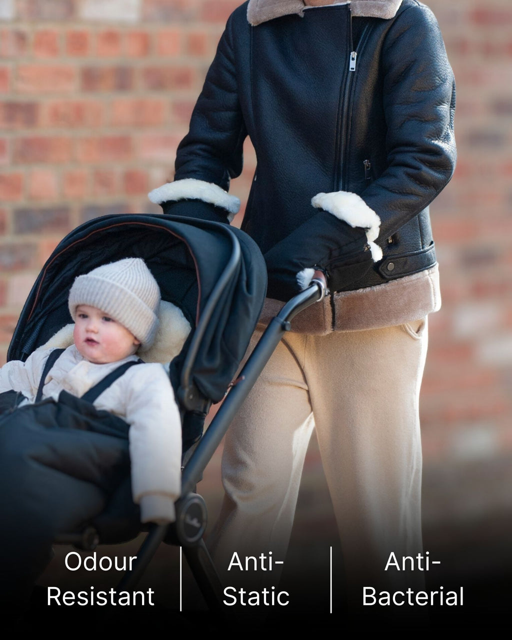 Person pushing a stroller with black sheepskin mittens attached to stroller.