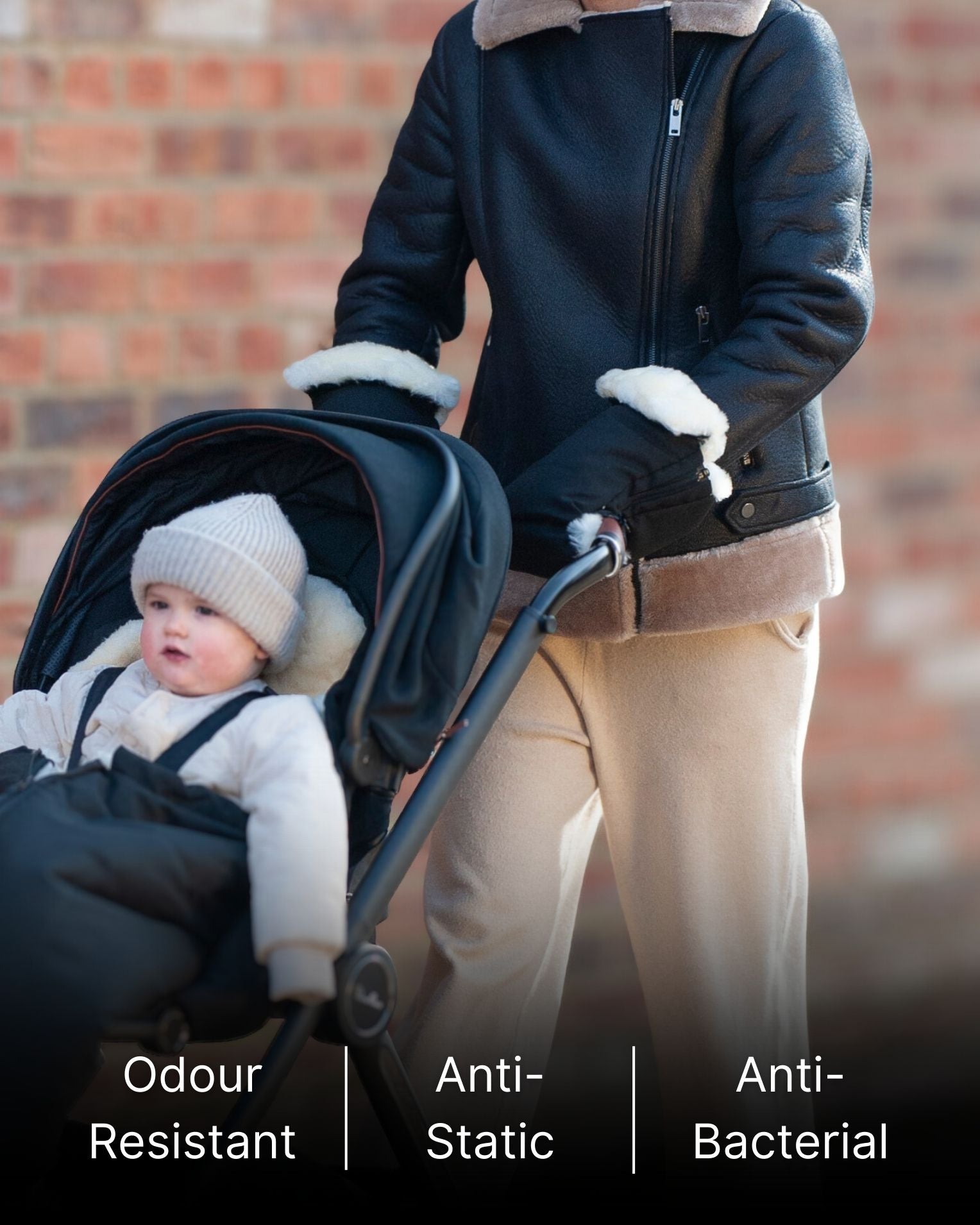 Person pushing a stroller with black sheepskin mittens attached to stroller.