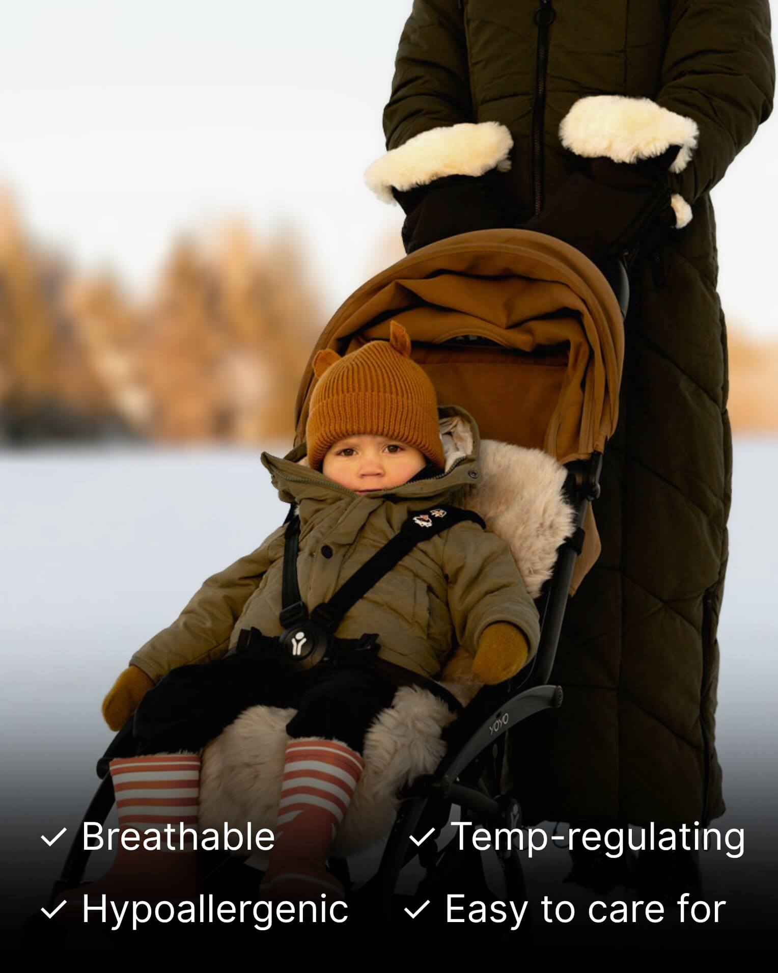 Child in a stroller being pushed with black sheepskin mittens attached to the stroller.