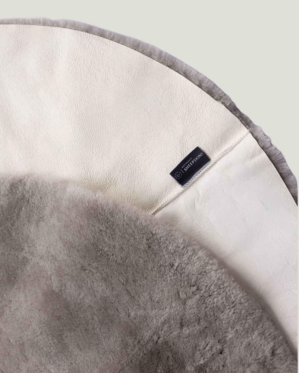 Close up of the back and front of a taupe round sheepskin playmat 