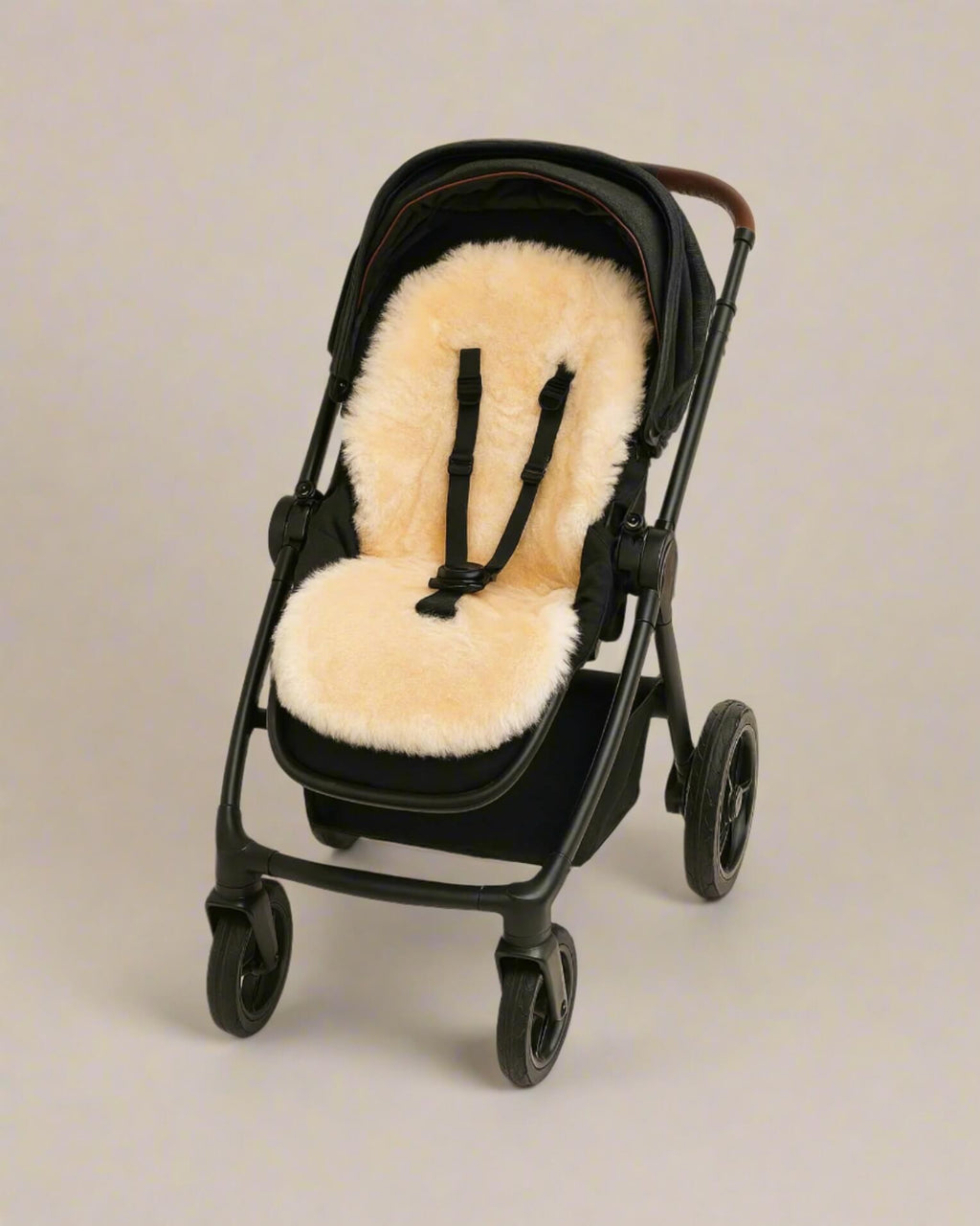 Black stroller with a beige sheepskin seat liner on a neutral background